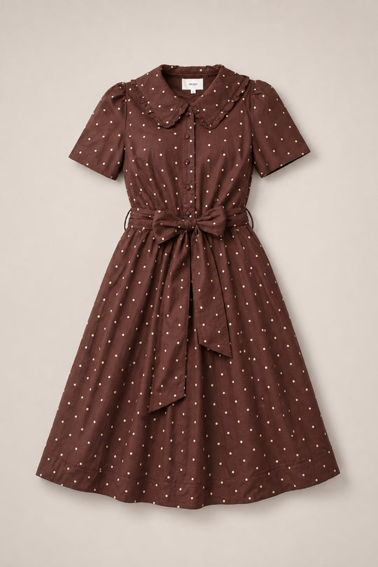The Kit Dress in Warm Cocoa Dainty Dot by Ivy City Co is a brown, knee-length cotton midi dress featuring white polka dots, short sleeves, a Peter Pan collar, a nursing-friendly button-down front, and a matching fabric belt that ties at the waist—capturing timeless charm in every detail.