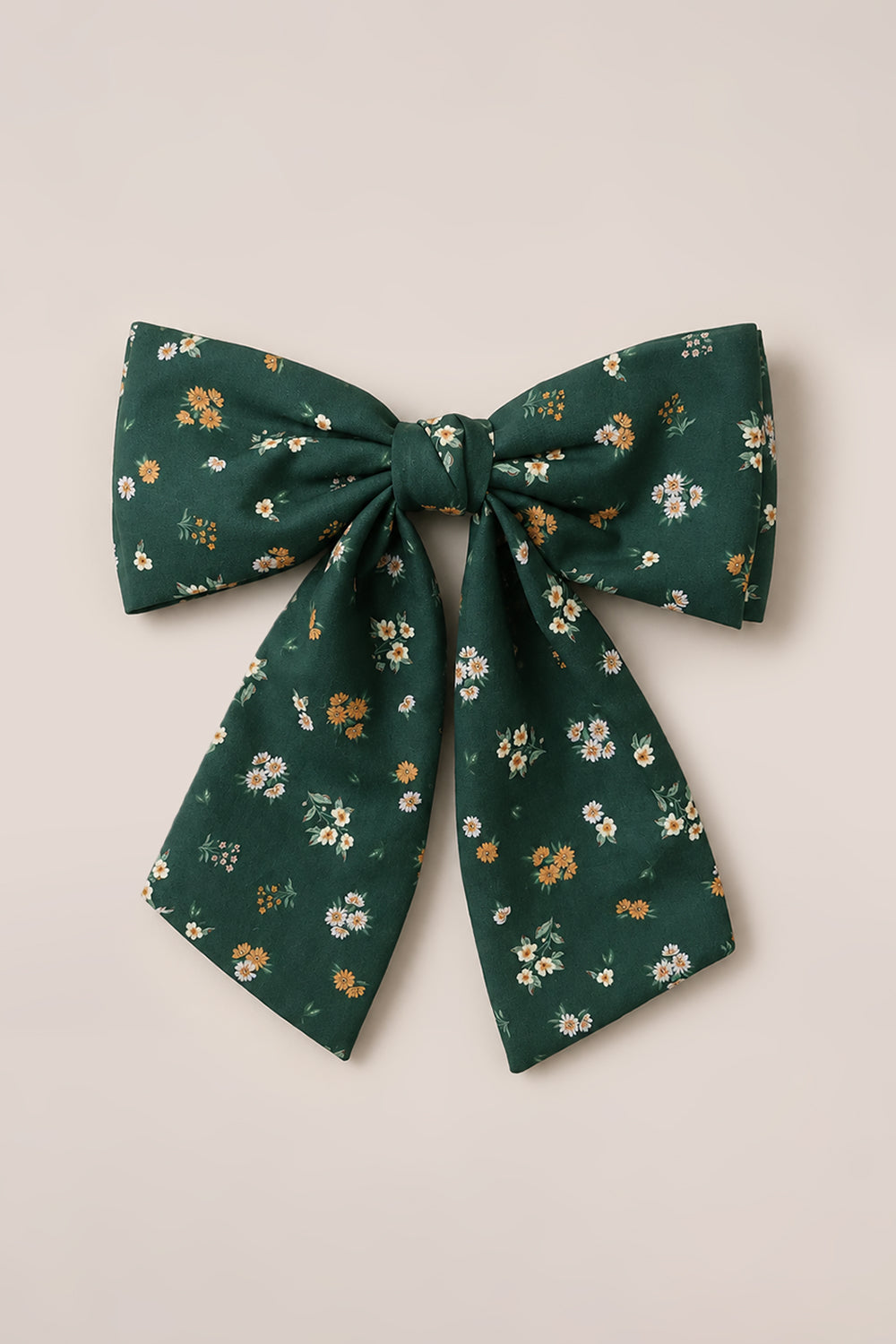 The Ivy City Co Hair Bow in Evergreen Lovelorn Ditsy—a large green fabric accessory adorned with a delightful blend of white, yellow, and orange floral motifs—is attractively showcased against a neutral background.