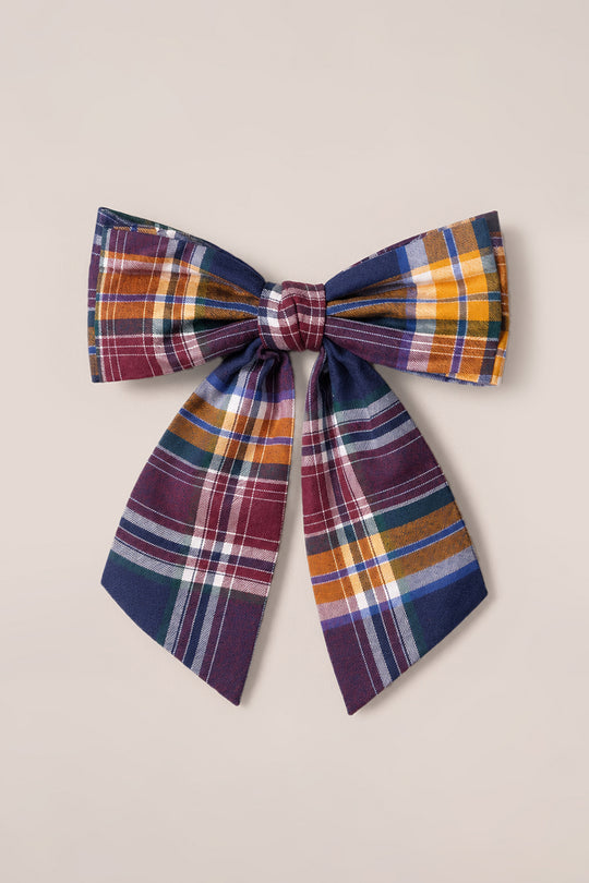 Discover the Ivy City Co Hair Bow in Midnight Plaid—a delightful cotton accessory adorned with wide loops and long tails. Showcasing a vibrant pattern of burgundy, yellow, green, white, and blue stripes against a light beige background, this charming hair bow is finished with a secure French barrette clip for easy styling.
