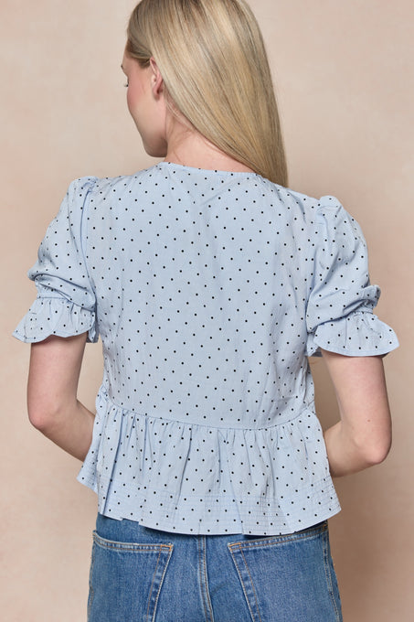 A woman with long blonde hair is shown from the back, wearing the Ivy City Co Lavinia Top in Light Blue paired with blue jeans.