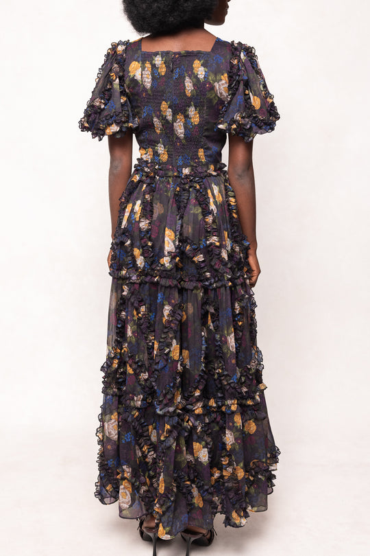 Woman wearing a dark floral dress with ruffled layers on a white background