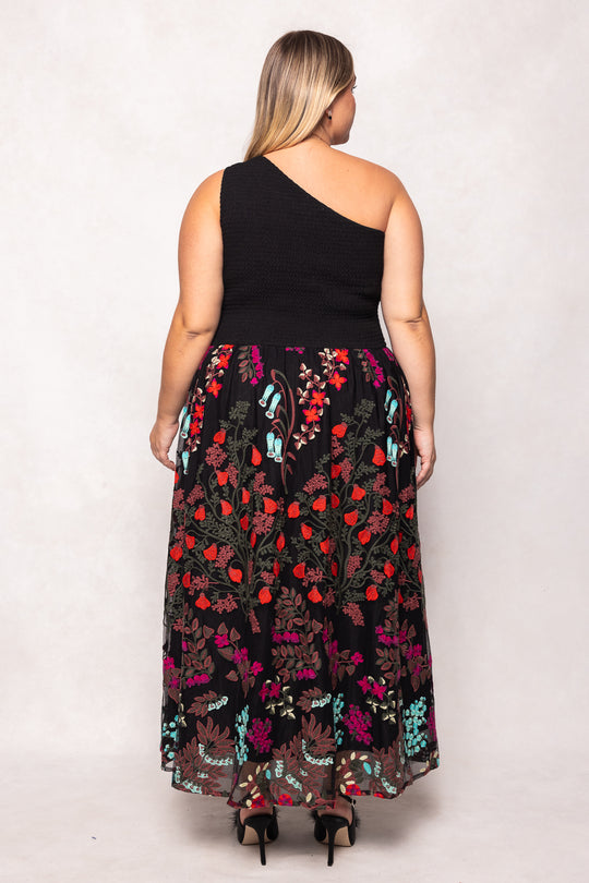 Woman wearing a black one-shoulder top with a colorful floral skirt on a white background