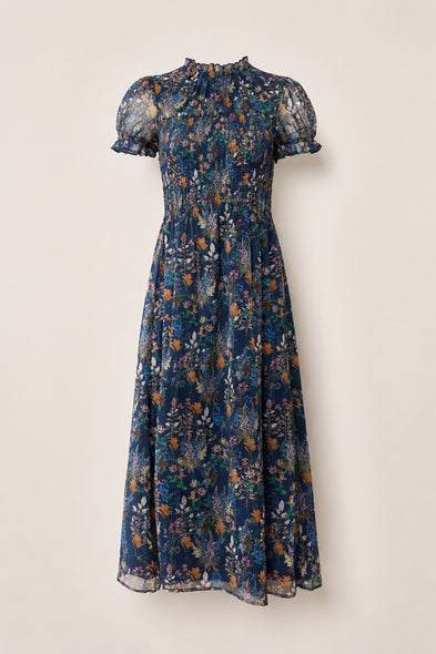 Discover the Leonora Dress in Midnight Autumn Bouquet by Ivy City Co—a navy blue, midi-length dress with short, sheer puff sleeves and a high ruffled collar. Featuring a beautifully smocked bodice, this elegant piece is decorated with an autumn-inspired floral print in orange, white, and green, and finished with a flowy skirt for effortless charm.