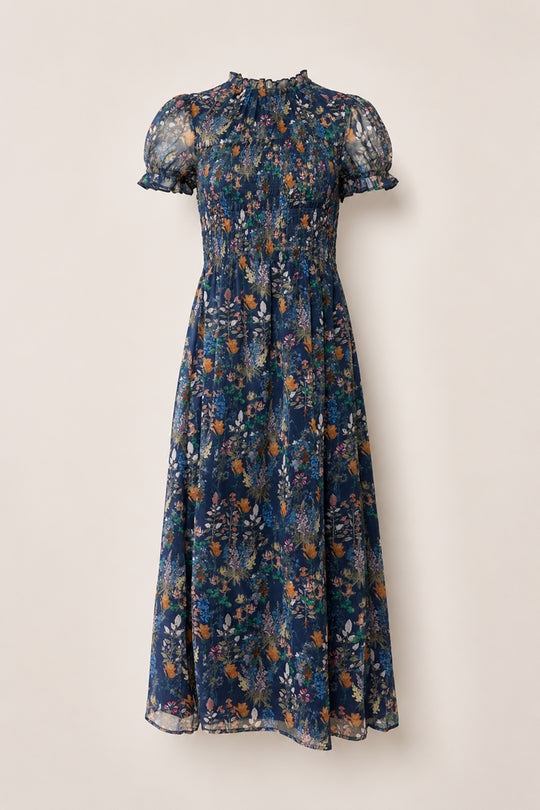 Discover the Leonora Dress in Midnight Autumn Bouquet by Ivy City Co—a navy blue, midi-length dress with short, sheer puff sleeves and a high ruffled collar. Featuring a beautifully smocked bodice, this elegant piece is decorated with an autumn-inspired floral print in orange, white, and green, and finished with a flowy skirt for effortless charm.