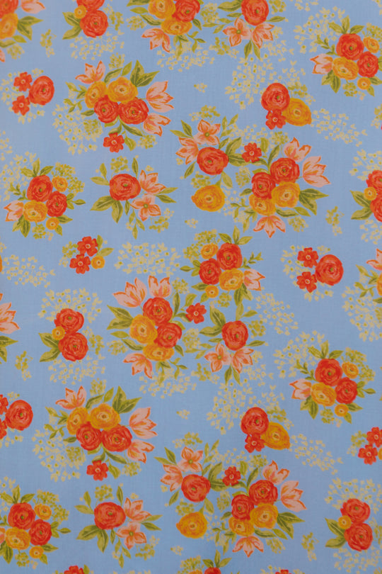 Inspired by Ivy City Cos Libby Dress in Orange Floral, this design features bright orange, red, and yellow flowers with green leaves scattered evenly across a light blue background for a cheerful look.