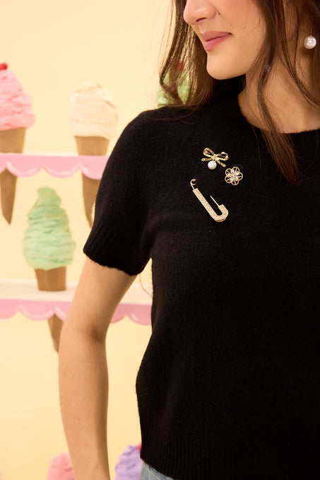 Person wearing a black shirt with decorative pins, standing in front of ice cream cone decorations.