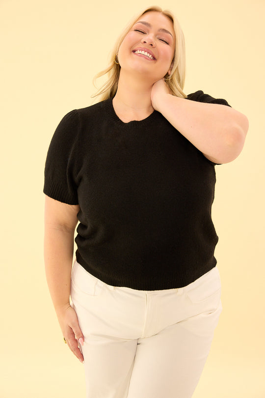 Woman wearing a black t-shirt and white pants on a beige background