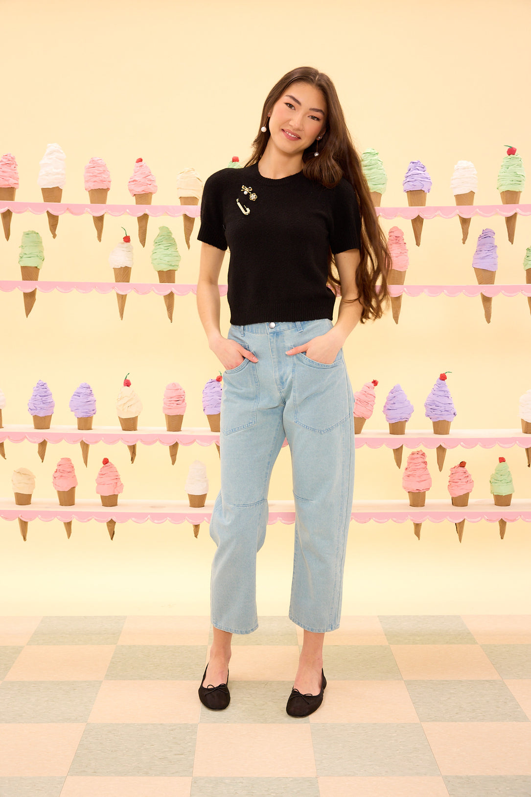 Woman in black t-shirt and light blue jeans standing in front of an ice cream-themed wall.