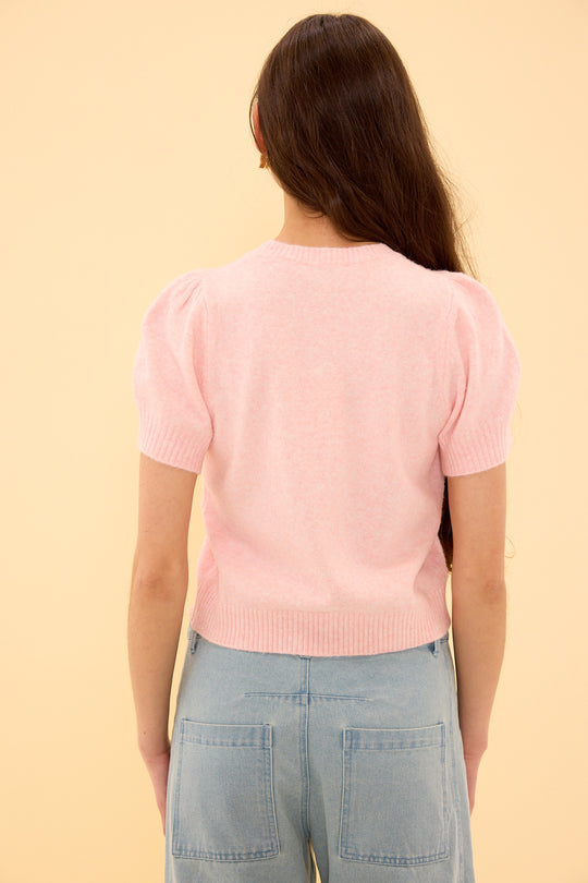 Person wearing a pink sweater and light blue jeans on a beige background