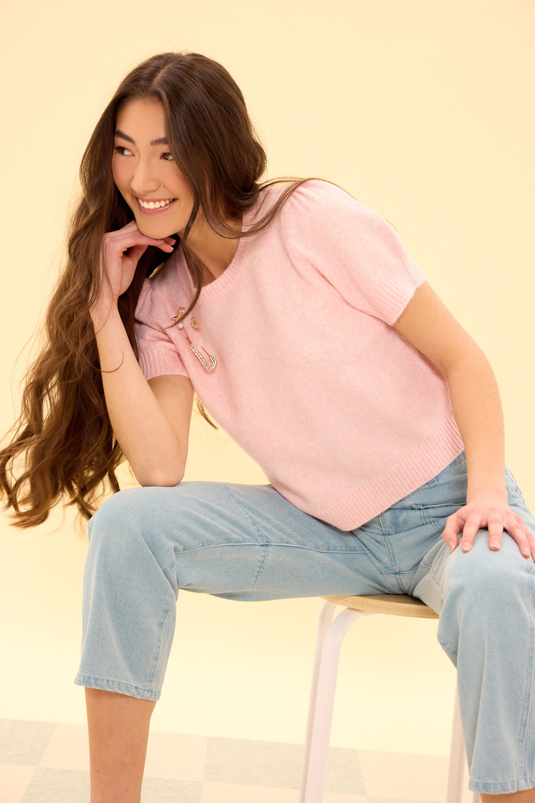 Woman sitting on a chair wearing a pink top and blue jeans against a beige background