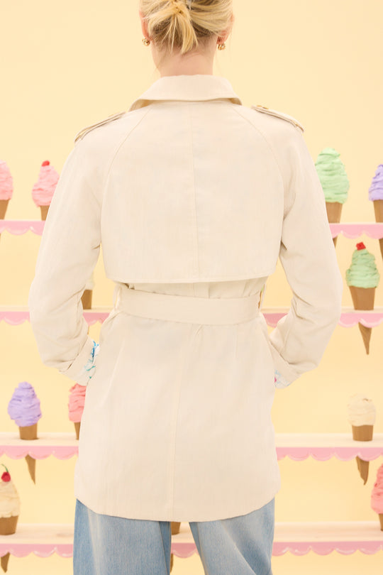 Person wearing a beige trench coat standing in front of ice cream cones on a yellow background