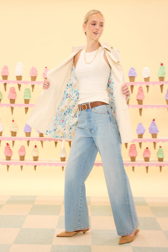 Woman in a floral top, white cardigan, and blue jeans standing in front of an ice cream cone display.