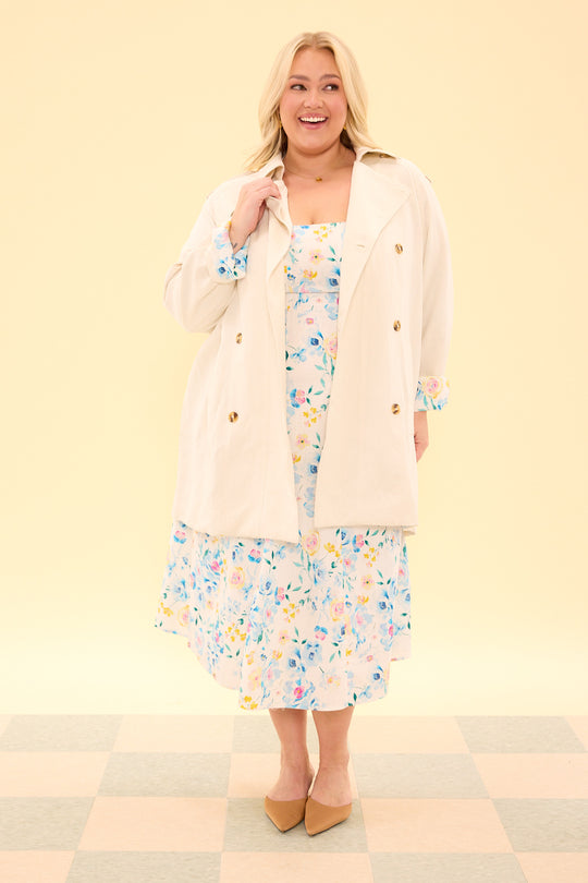 Woman wearing a floral dress with a beige cardigan on a light yellow background
