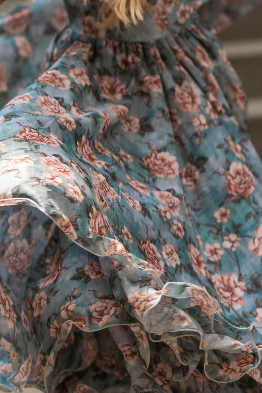 A close-up of the Lisette Dress in Rose Dusk by Ivy City Co, featuring flowing blue fabric adorned with a pink floral pattern and ruffled detailing in motion—perfect for creating a romantic fall wedding look.