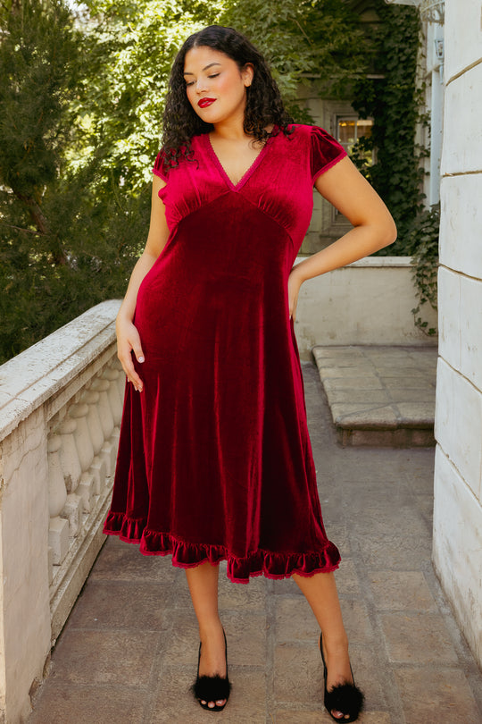 Red velvet dress on a woman on a patio with greenery behind in the background