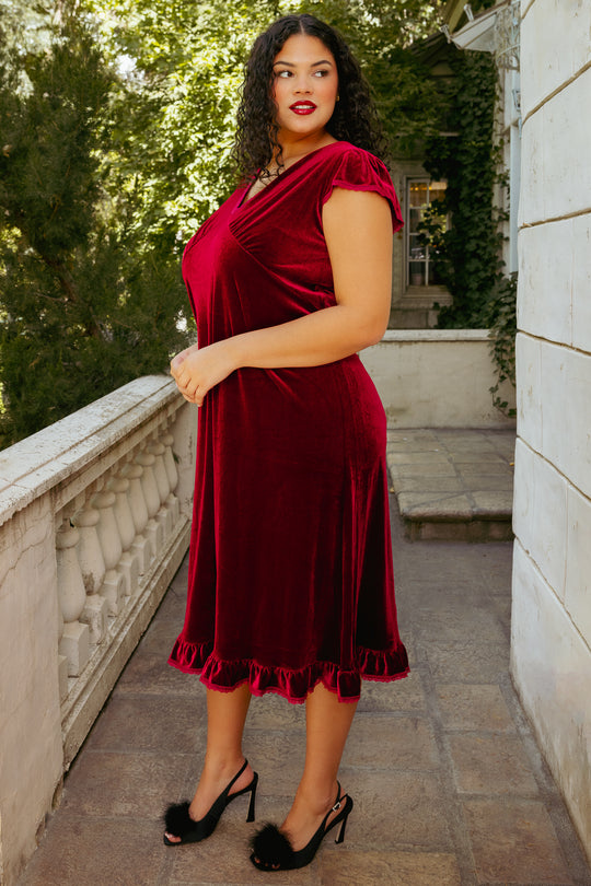 Red velvet dress on a woman on a patio with greenery behind in the background