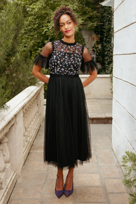 Woman wearing a black dress with floral embellishments in an outdoor setting.