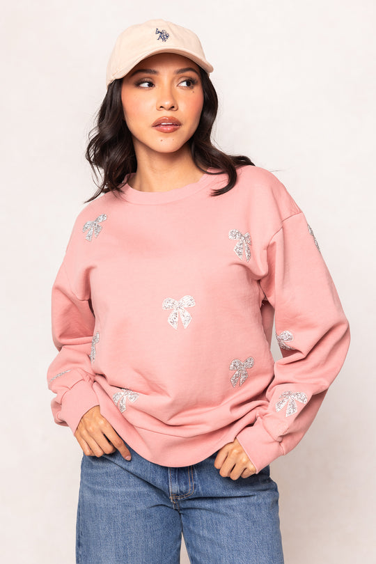 Woman wearing a pink sweatshirt with floral embellishments and a beige cap against a plain background