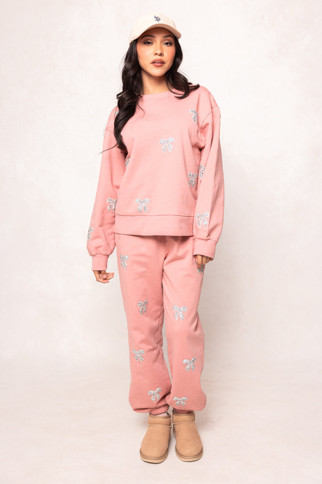 Person wearing a pink outfit with a matching cap and beige boots on a white background