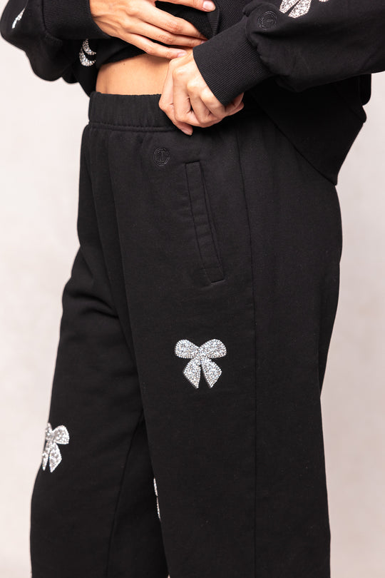 Black pants with bow embellishments on a light gray background