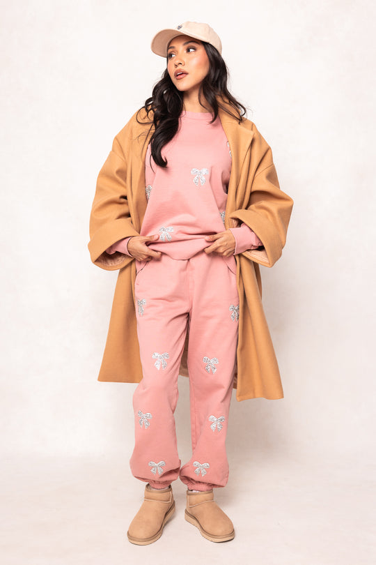 Woman wearing a tan coat, pink outfit with butterfly patterns, and beige boots on a white background