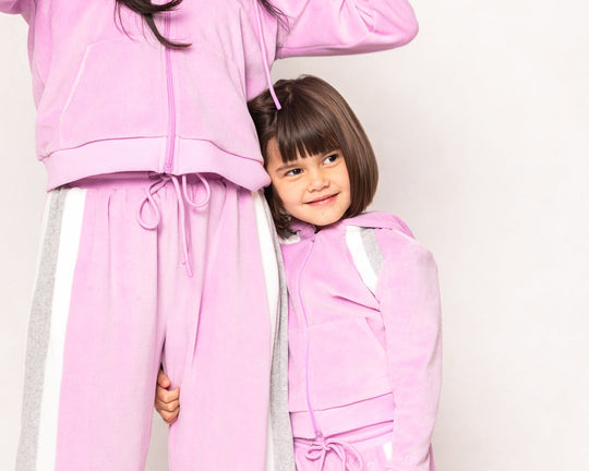 Two people wearing matching pink tracksuits on a plain background