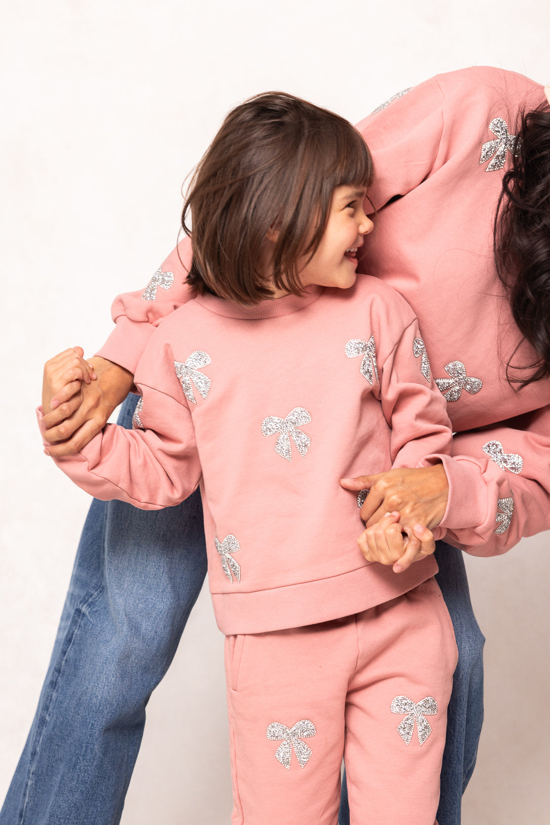 girl in a pink sweatsuit against a white background with her mom