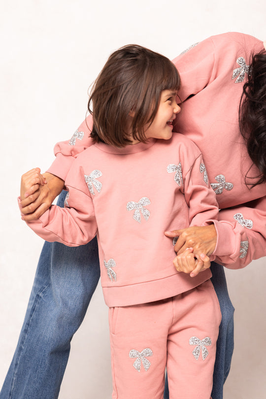 girl in a pink sweatsuit against a white background with her mom