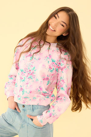 Woman wearing a pink floral sweatshirt and light blue jeans on a beige background