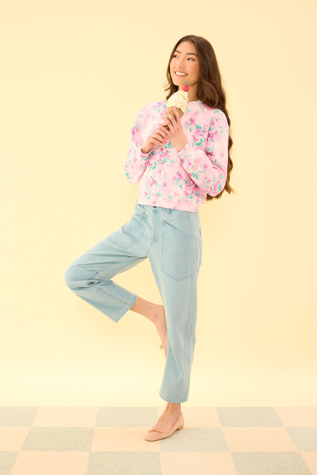 Woman wearing a floral blouse and light blue jeans on a yellow background