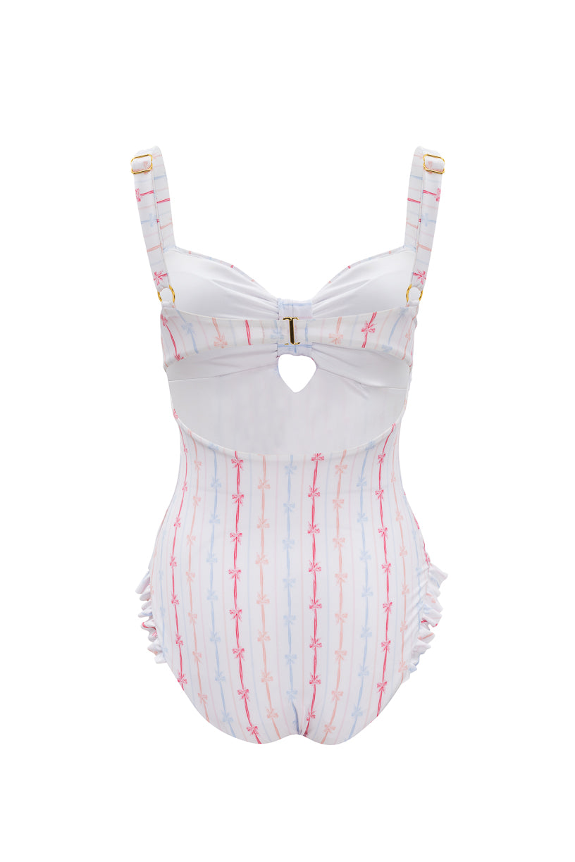 The Ivy City Co Lucy One Piece in Breea Bow features white fabric with pink and blue stripes, supportive straps, a front keyhole cutout, gold buckle at the bust, and subtle ruffle accents at the sides for a playful look.