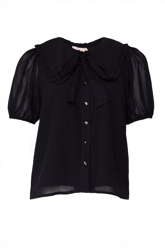 The Andrea Blouse in Black Chiffon by Ivy City Co features short sleeves with sheer puff detailing, a large ruffled collar, front buttons, and a matching bow tied at the neck.