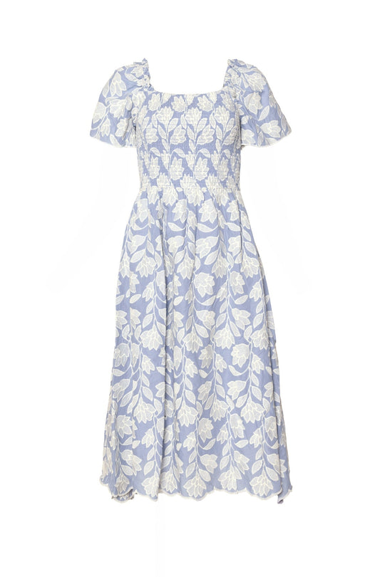 The Ophelia Dress in Mosaic Embroidery by Ivy City Co features a light blue midi length adorned with white floral patterns, short puffed sleeves, a smocked bodice, and a flared skirt. Displayed on a plain white background, this effortlessly stylish summer party dress is as maternity friendly as it is elegant.