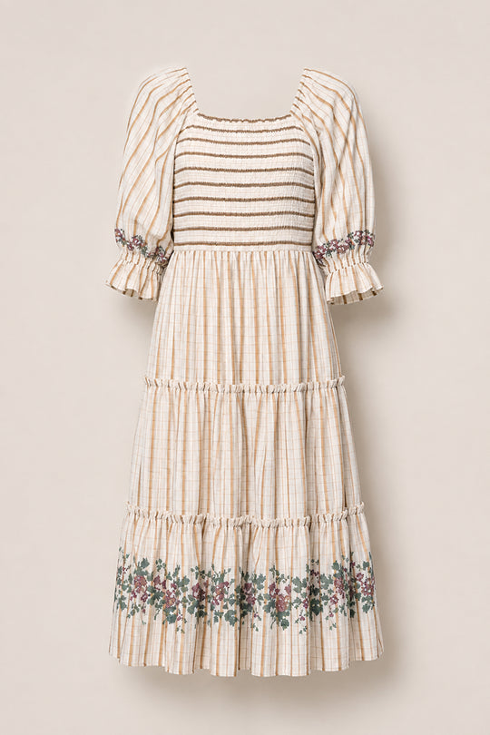 Introducing the Madeline Dress in Embroidered Cider Grid by Ivy City Co: a cream-colored midi dress designed with puffed sleeves, a smocked bodice, and a tiered skirt highlighted by delicate floral embroidery at the hem. The fabric showcases a subtle cider grid plaid pattern for added charm. Maternity friendly and effortlessly elegant, this dress is photographed against a plain light background.