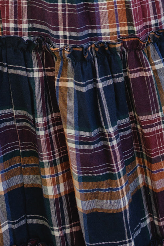 Close-up of fabric from the Ivy City Co Madeline Dress in Midnight Plaid, featuring a multicolored plaid pattern in shades of navy, orange, white, and purple, with gathered detailing along a seam and a smocked bodice for a comfortable, maternity-friendly fit.