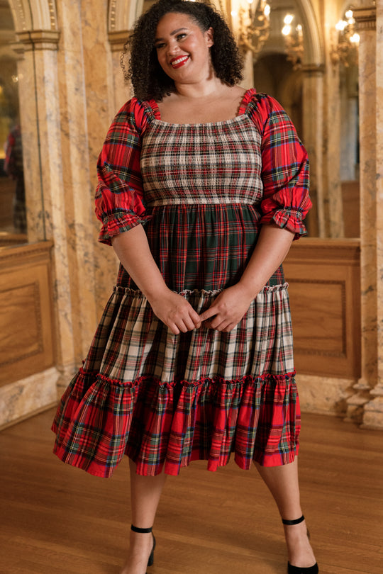 A woman stands smiling in an ornate room with marble walls, wood paneling, and mirrors, wearing the Ivy City Co Madeline Dress in Mixed Plaid with puffed sleeves.