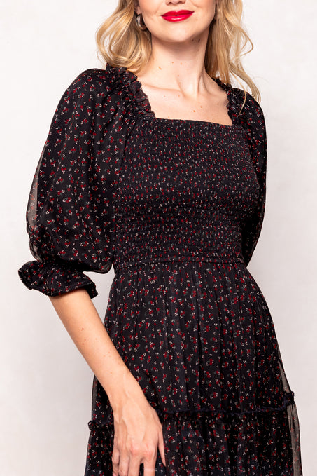 Woman wearing a black floral dress with sheer sleeves against a white background
