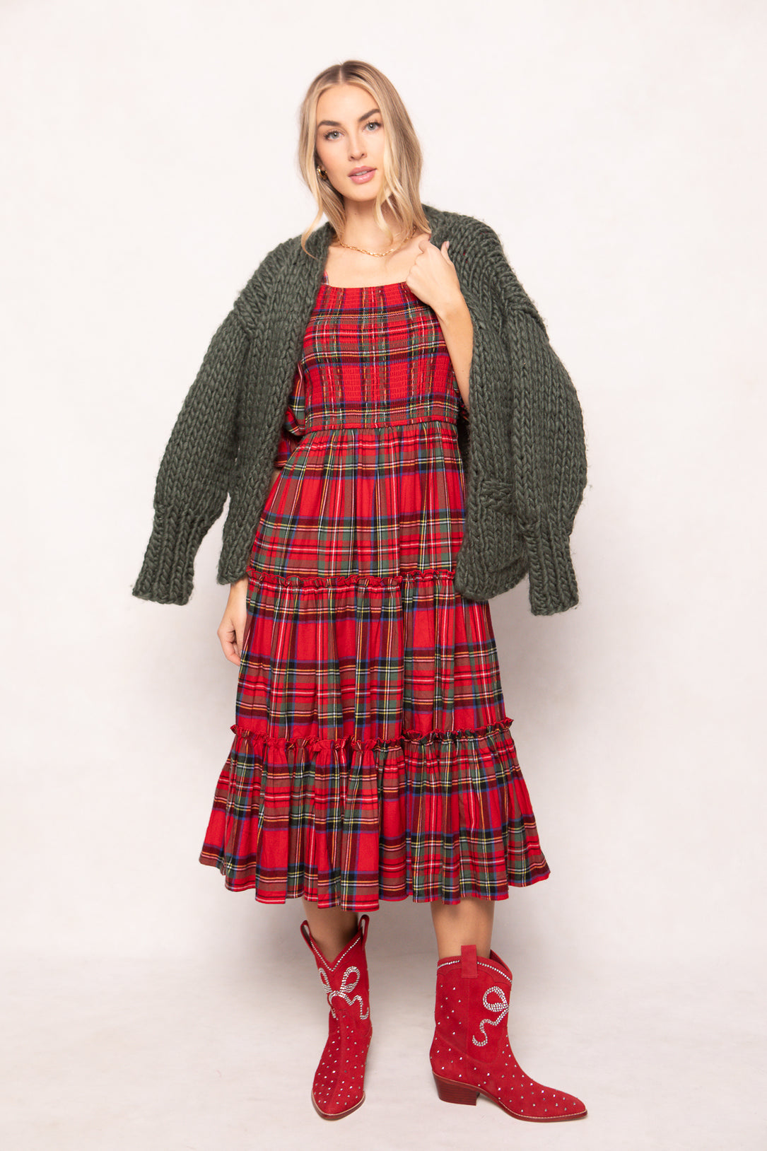 woman in a red plaid dress with red boots, and a green chunky cardigan on a white background 