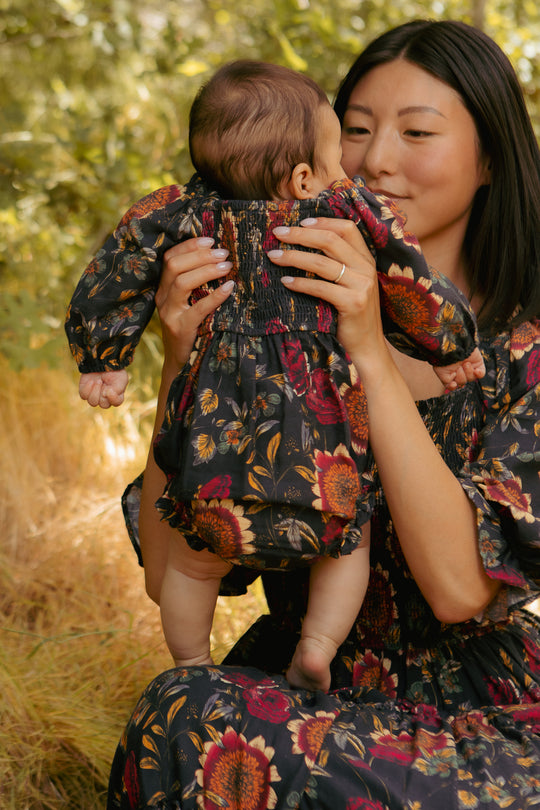 Woman holding a baby both wearing floral outfits in a natural setting
