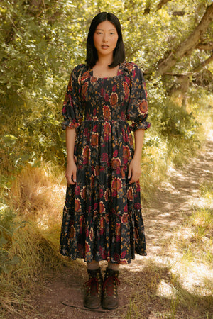 Woman in a patterned dress standing on a path surrounded by trees