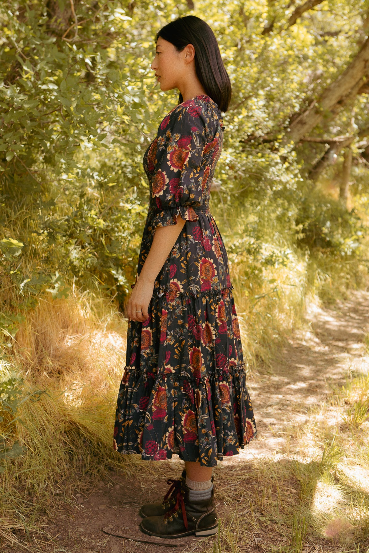 Woman in a floral dress standing in a sunlit forest