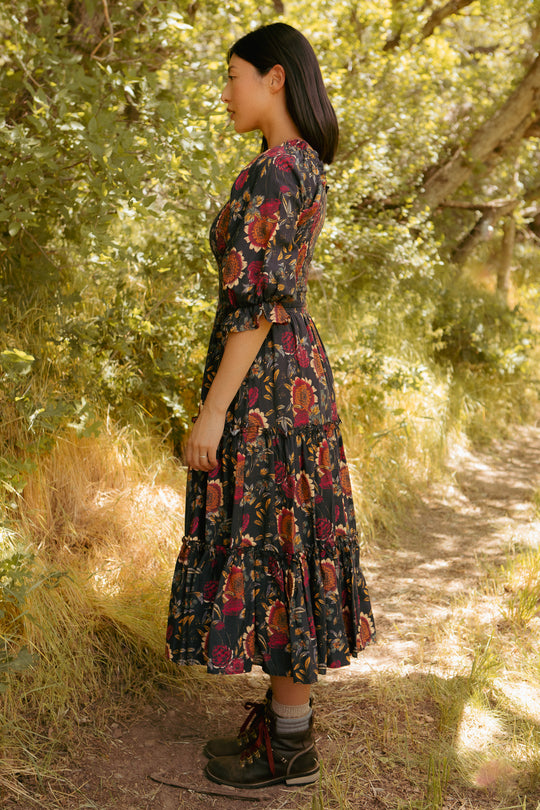 Woman in a floral dress standing in a sunlit forest