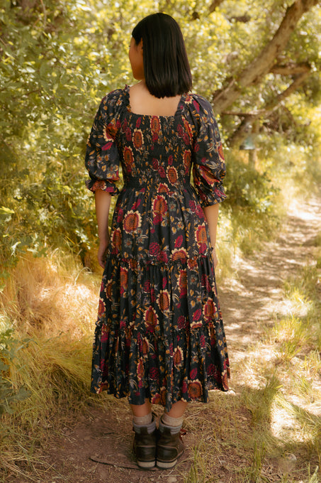 Woman in a patterned dress standing on a path surrounded by trees