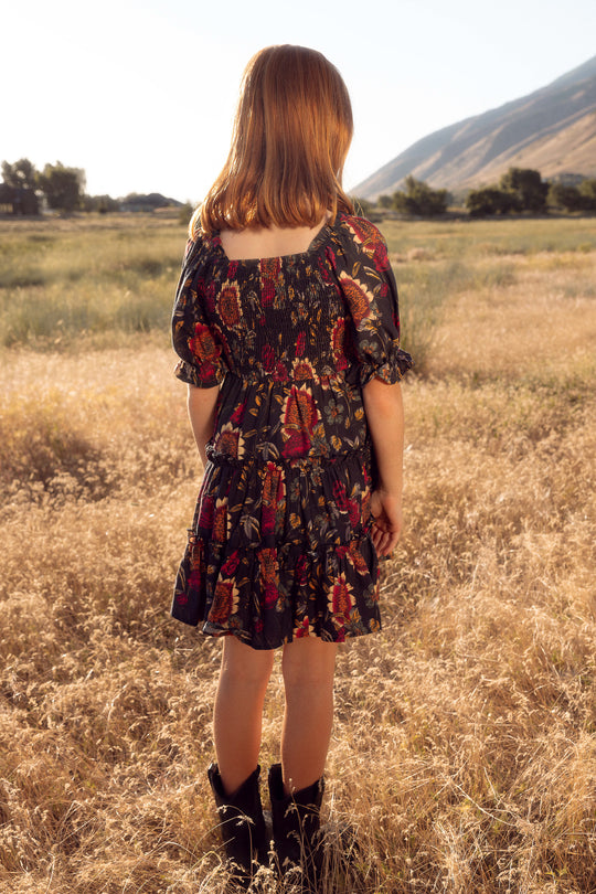 Woman in a patterned dress standing in a field with mountains in the background