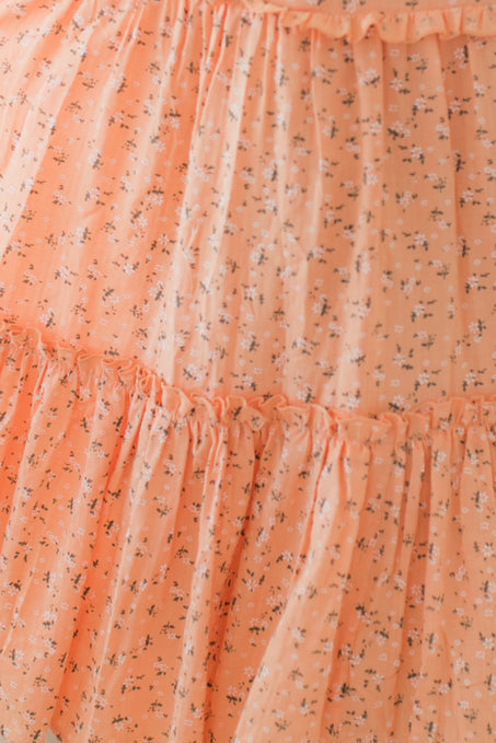 Close-up of the Madeline Dress in Sorbet by Ivy City Co.—a peach sheer maternity dress adorned with small florals, featuring a smocked bodice and gathered ruffled tiers.