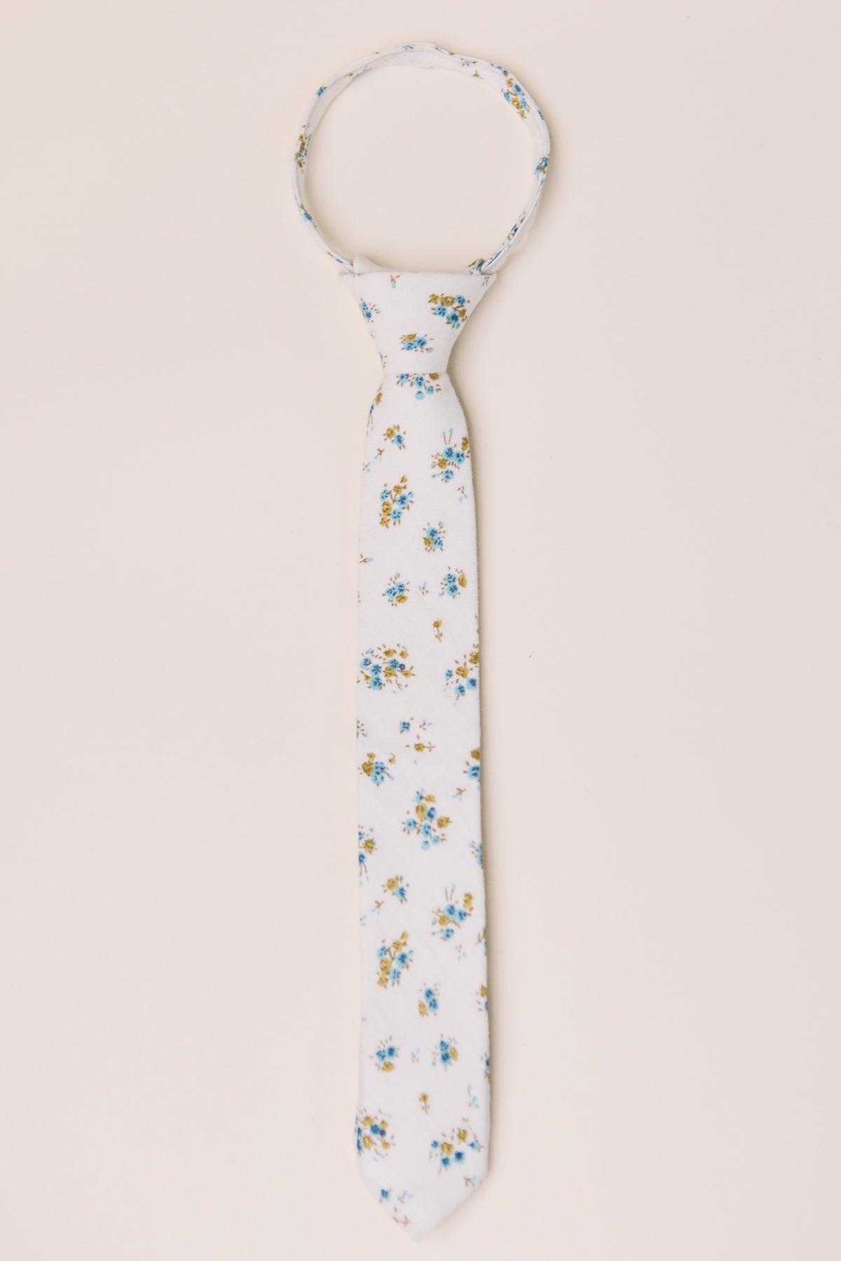 The Ties in Madeline Blue Floral by Ivy City Co feature a white base with blue and yellow flowers, shown flat on a beige background. Ideal for family matching or pairing with a boys bow tie.