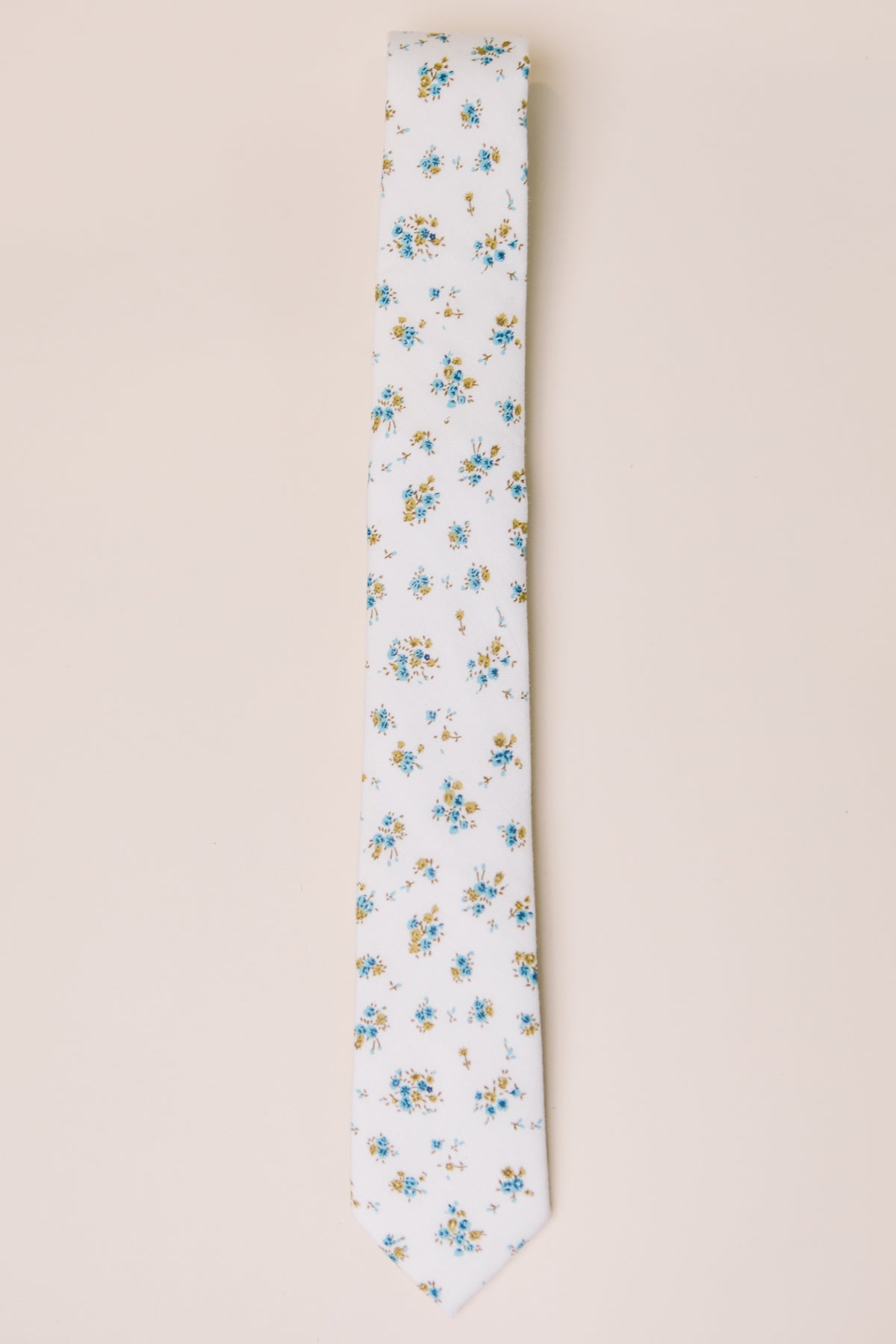 The Ivy City Co Ties in Madeline Blue Floral feature a white base with blue, yellow, and green floral accents—ideal for family matching—shown on a light beige background.