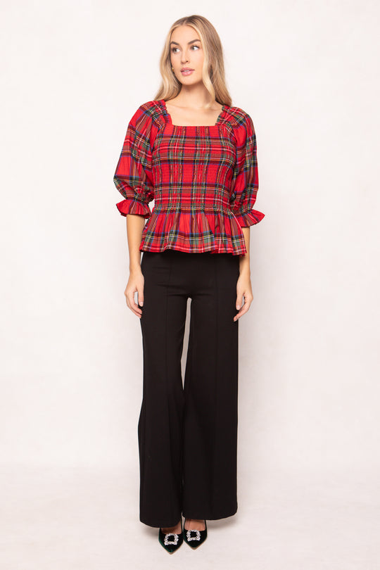 woman wearing a red plaid top with black pants and heels on a white backdrop 