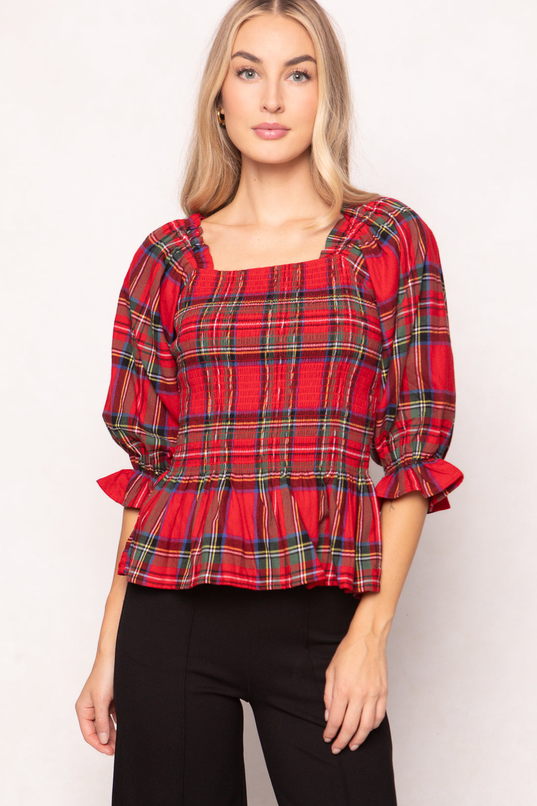 woman wearing a red plaid top with black pants and heels on a white backdrop 