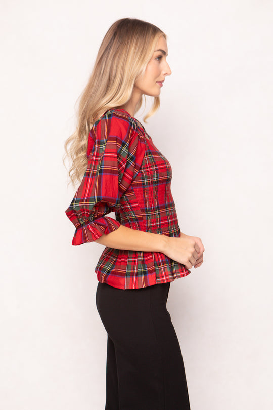 woman wearing a red plaid top with black pants and heels on a white backdrop 